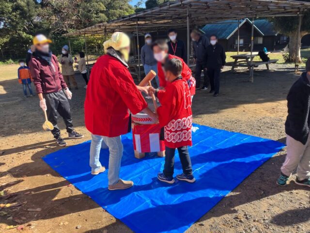 法被を着た子どもが大人と一緒に杵を持って餅をつく様子